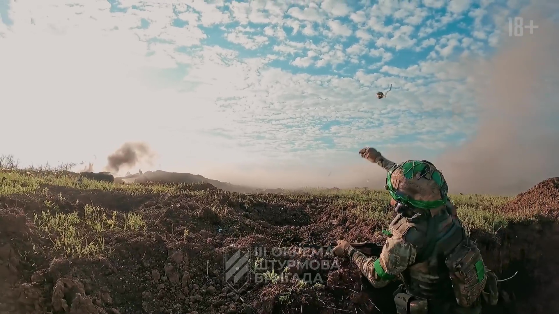 Un soldat en tenue de combat, de dos, en train de lancer une grenade au loin depuis une tranchée. Le ciel est bleu, ensoleillé, rempli de petits nuages, et l'herbe d'un vert tendre.