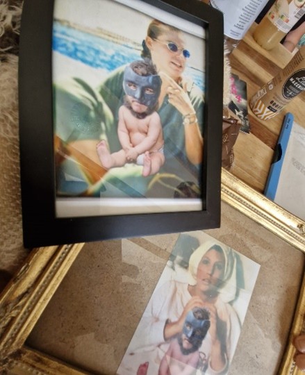 Dans un cadre, la photo d'une femme qui tient sur ses genoux un bébé en couche avec un masque sur la tête.